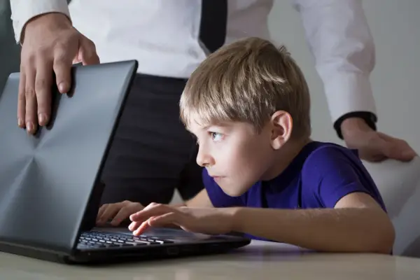 Chłopiec pochłonięty grą na laptopie, a dorosły próbuje go odciągnąć. Czy to początek uzależnienia od internetu?