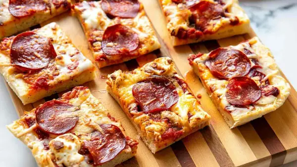 Kawałki pizzy pepperoni na desce. Dowiedz się, jak podgrzać pizzę na patelni, by była idealnie chrupiąca.