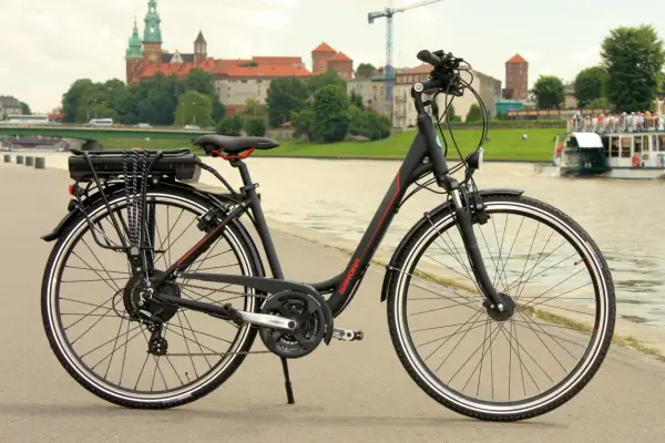 Czarny rower elektryczny z baterią na bagażniku, gotowy do jazdy po bulwarach z widokiem na Wawel.