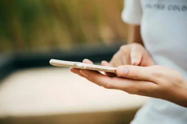 Dłonie trzymające złoty telefon. Zastanawiasz się, jak wyczyścić telefon? Oto praktyczny poradnik.