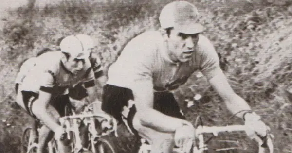 Dwóch kolarzy w akcji. Na pierwszym planie widać zawodnika w czarnych spodenkach i jasnej koszulce, zdeterminowanego jak zawsze Eddy Merckx.
