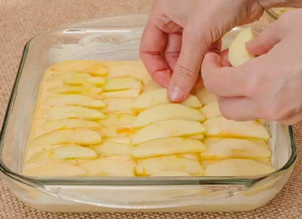 Ręce układają plasterki jabłek na cieście. Powstaje pyszne ciasto z jabłkami, gotowe do pieczenia.