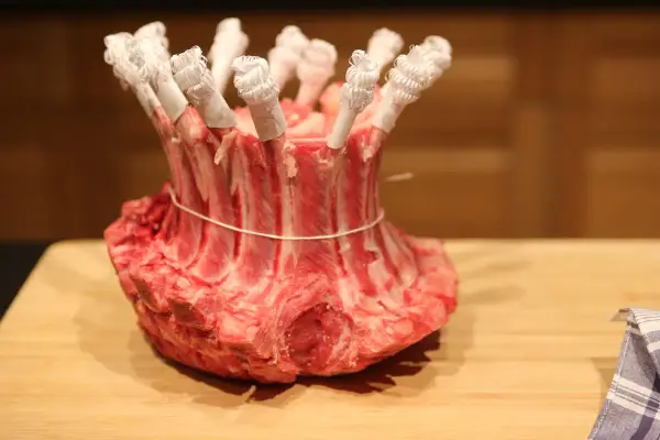 Une couronne d'agneau crue, prête pour la cuisson, avec les os protégés par du papier blanc.