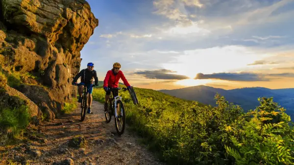 Dwóch rowerzystów przemierza górski szlak o zachodzie słońca, odkrywając piękno krajoznawstwa.
