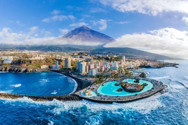 Città costiera con piscina a sfioro e vulcano sullo sfondo. Un'ottima idea su dove andare ad aprile per una vacanza al mare.