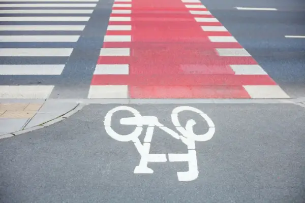 Czerwone pasy dla rowerzystów przecinają przejście dla pieszych. Symbol roweru na asfalcie zaprasza do bezpiecznej jazdy.