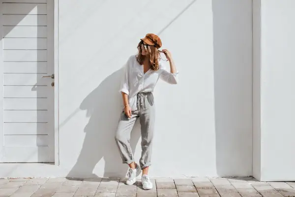 Modello con cappello marrone e occhiali da sole, indossa una camicia bianca e pantaloni grigi. Un esempio di abbinamenti outfit grigio casual e chic.
