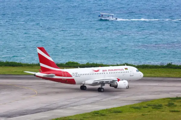 Samolot Air Mauritius na pasie startowym, w tle turkusowe morze i łódź. Twoje loty na Mauritius właśnie się zaczynają!