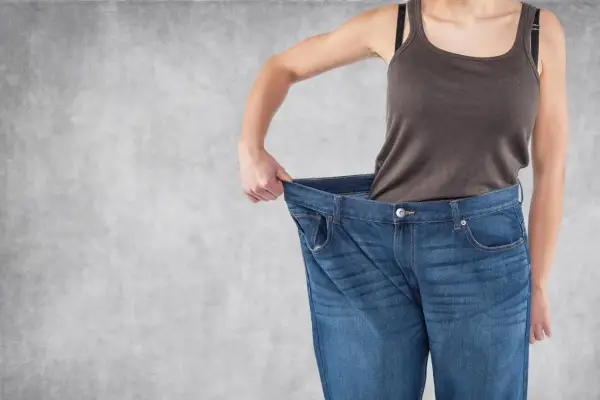 Erfolg beim Gewichtsverlust: Eine Person hält ihre viel zu große Jeans hoch, ein deutliches Zeichen für erreichten Gewichtsverlust.