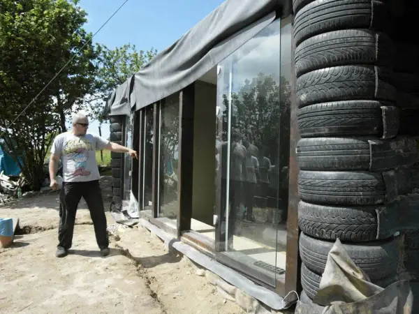 Budowa **earthship** z opon. Mężczyzna wskazuje na szklaną ścianę domu z opon.