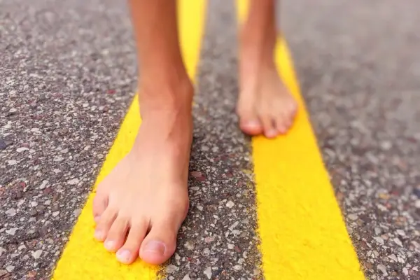 Piedi nudi che camminano su una strada con strisce gialle. Un'esperienza di correre scalzi per sentire la strada.