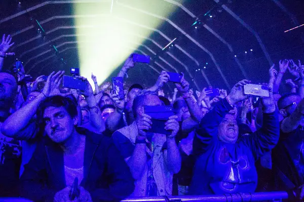 Tłum na fest festiwalu nagrywa koncert telefonami. Światła sceny oświetlają twarze ludzi.