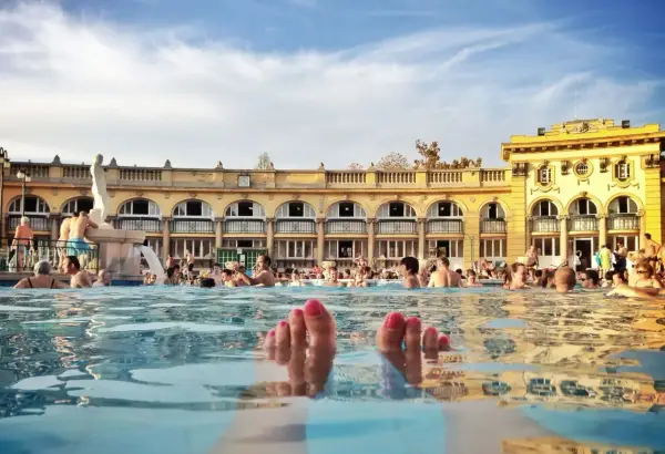 Fötter sticker upp ur vattnet i ett soligt budapest spa. Människor badar och njuter av den vackra arkitekturen.