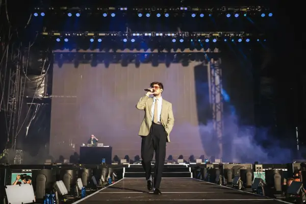 Taco Hemingway na scenie, w garniturze i z mikrofonem. Koncertowy klimat, światła i dym. To musi być koncert Taco Hemingway 2026!