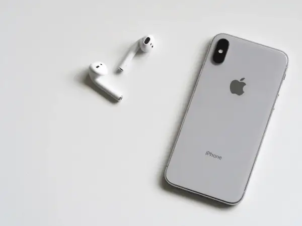 Srebrny iPhone i białe słuchawki AirPods leżą na białym tle. Może rozmówca na iPhonie słabo słychać?