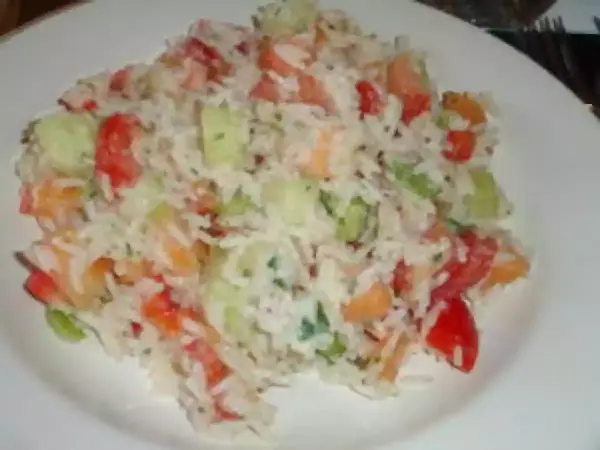 Une savoureuse salade de riz garnie de dés de tomates, de concombre et d'herbes fraîches, servie sur une assiette blanche.