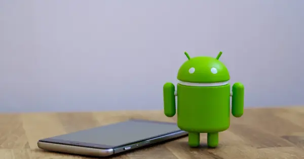 Zielony robot Android obok telefonu, symbolizujący najnowszą wersję systemu android 14.