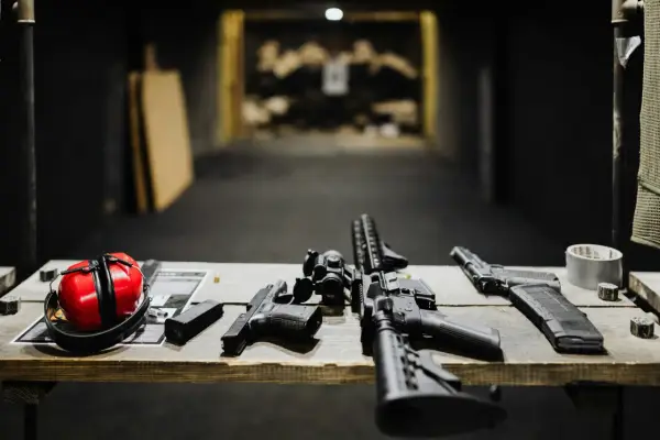 Na stole leżą pistolety, karabin, magazynki i czerwone nauszniki. To przygotowanie do egzaminu na pozwolenie na broń.