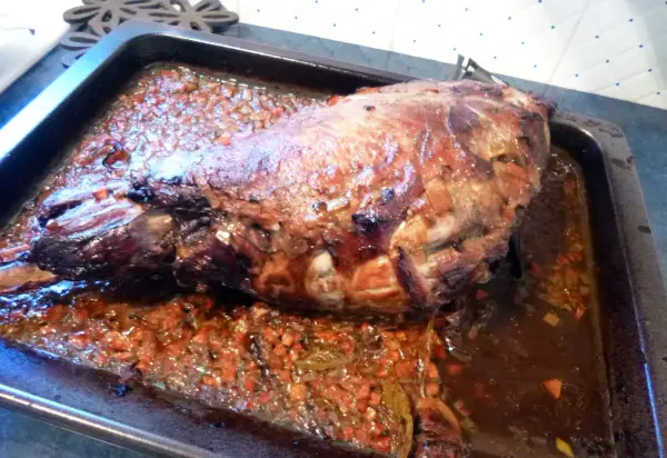 Gigot de sanglier rôti 7h, baignant dans son jus avec des légumes coupés. Un plat savoureux prêt à être dégusté.