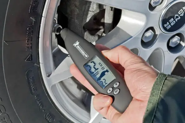 Mano usa un medidor digital Michelin para comprobar la **pegatina presión neumáticos** de un coche.