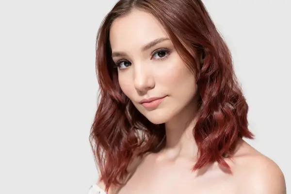 Mahoń kolor włosów komu pasuje? Modelka z rudymi, falowanymi włosami prezentuje ten odcień.