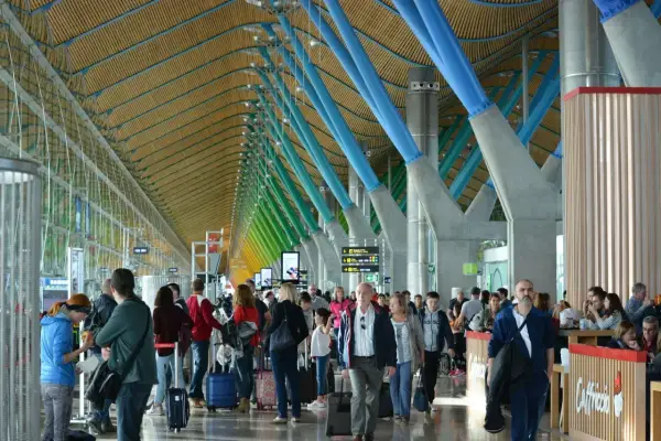 Ludzie z bagażami w nowoczesnym terminalu, jednym z wielu lotnisk w Europie, podziwiają architekturę z kolorowymi podporami.