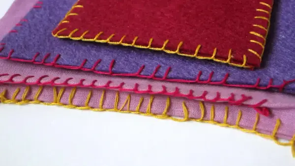 Tessuti colorati sovrapposti, rifiniti con un punto coperta giallo, rosa e rosso.
