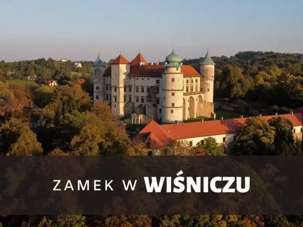 Majestatyczny zamek Wiśnicz otoczony jesiennymi drzewami, z charakterystycznymi wieżami i czerwonymi dachami.