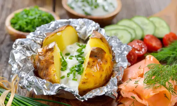 Pommes de terre à la braise, enveloppées dans du papier aluminium, garnies de crème et de ciboulette. Parfait pour le temps de cuisson.