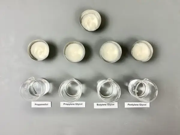 Sześć próbek kremów w małych pojemnikach i cztery zlewki z płynami: propanediol, glikol propylenowy, **butylene glycol** i pentylene glycol.