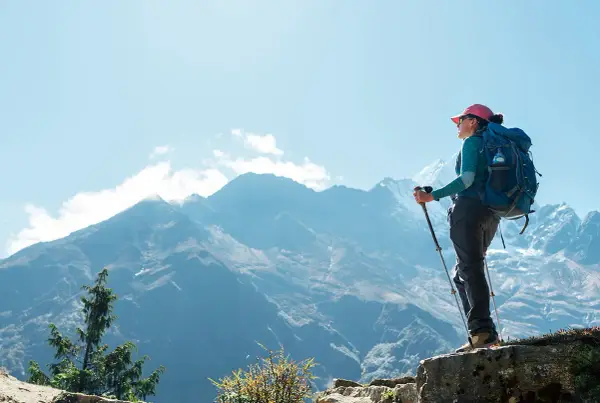 Kobieta z plecakiem i kijkami trekkingowymi na tle gór, w drodze do **base camp Everest**.