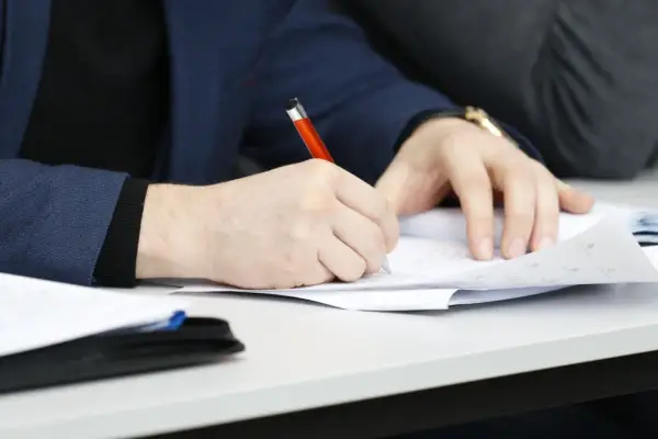 Ręka pisze długopisem po papierze, przygotowując przykładowy artykuł po angielsku na maturę.