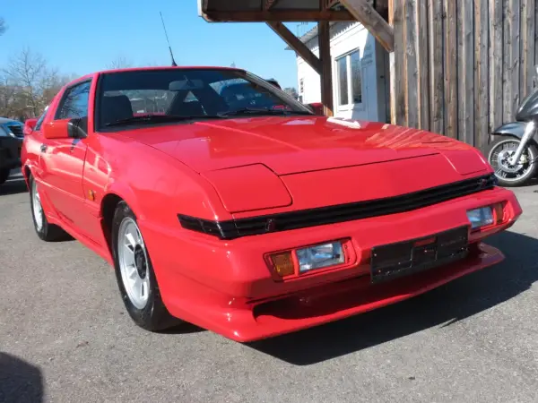 Czerwony Mitsubishi Starion z lat 80. błyszczy w słońcu. Klasyk sportowy z wysuwanymi światłami.