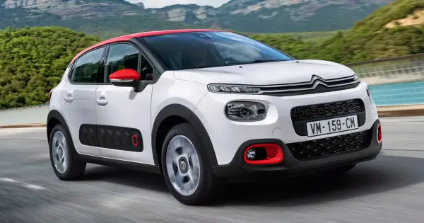 Biały Citroen C3 2025 z czerwonym dachem i lusterkami jedzie po drodze, otoczony zielonymi wzgórzami.
