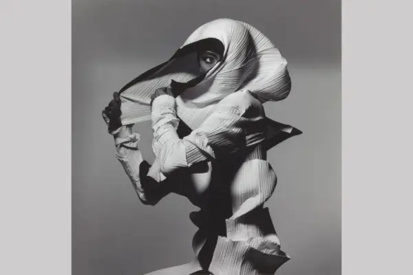 Modella con un abito plissettato bianco, un'opera d'arte di Irving Penn, che nasconde il viso tranne un occhio penetrante.