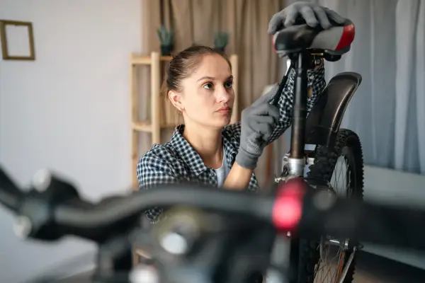 Kobieta w rękawiczkach reguluje sztycę rowerową, sprawdzając jej rozmiary.