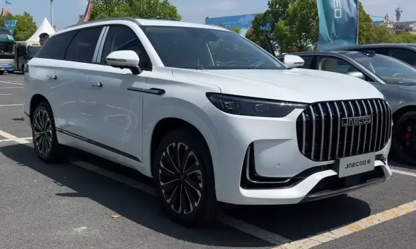 Biały SUV Jaecoo 9 z chromowanym grillem i czarnymi felgami stoi na parkingu.