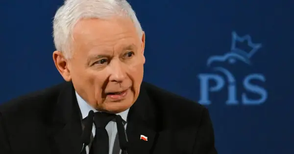 Jarosław Kaczyński, w garniturze z polską flagą, przemawia na tle logo PiS. Czy Jarosław Kaczyński faktycznie planuje oddać władzę młodszym politykom?