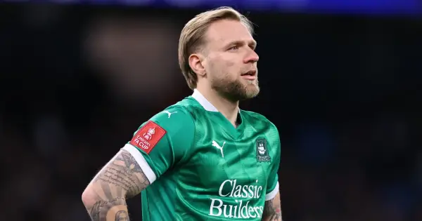 Piłkarz w zielonej koszulce z herbem klubu i naszywką FA Cup. Widać tatuaże na ramieniu. To właśnie tam gra puchacz.