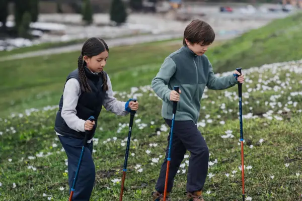 Dzieci z kijkami trekkingowymi idą przez kwitnącą łąkę. W tle widać resztki śniegu, co sugeruje wczesną wiosnę w Tatrach zimą z dzieckiem.