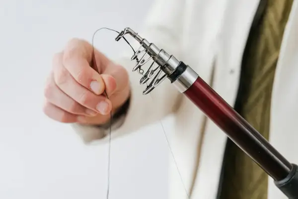 Dłoń przygotowuje żyłkę do zarzucenia, pokazując podstawowe węzły wędkarskie na końcu wędki.