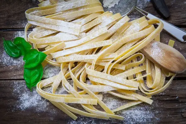 Świeży makaron tagliatelle posypany mąką, z listkami bazylii i drewnianą łyżką.