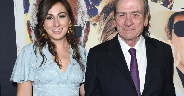 Tommy Lee Jones z żoną, uśmiechnięci na tle plakatu filmowego.