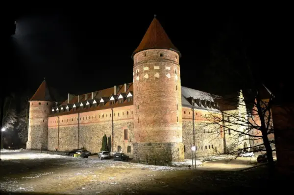 Zamek w Bytowie nocą, oświetlony, z wieżami i kamiennymi murami.