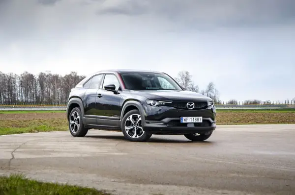 Czarna Mazda MX-30 na tle pochmurnego nieba i drzew.
