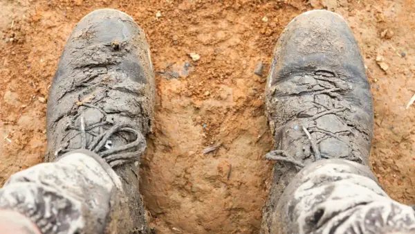 Mud-caked boots, laces frayed, look like they're falling apart after a tough hike.
