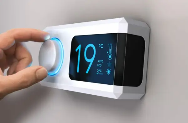 Main d'une personne ajustant le réglage de température sur un cee thermostat connecté affichant 19°C.