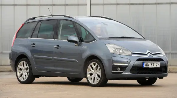 Szary Citroen C4 Grand Picasso 2.0 HDI z kierowcą za kierownicą, zaparkowany przed budynkiem.