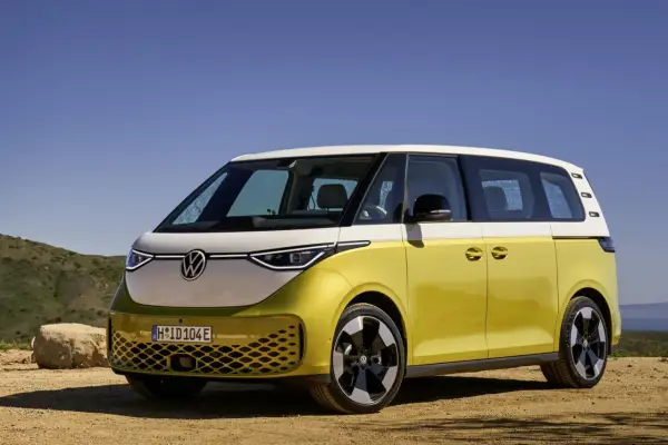 Minivan elettrico Volkswagen ID. Buzz bicolore giallo e bianco, parcheggiato su un terreno sterrato con sfondo di colline e cielo azzurro.