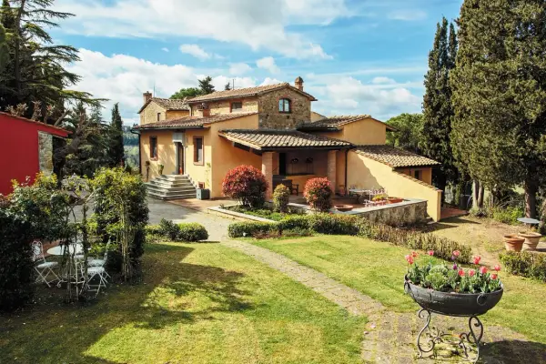 Un perfetto weekend in Toscana: villa con giardino fiorito, cipressi e un cielo azzurro con nuvole bianche.